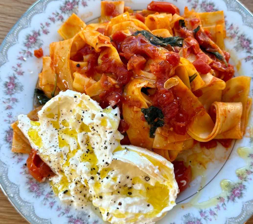 A close-up of pappardelle pasta with slow-cooked tomato sauce and a fresh burrata ball, cooked in a pink Lynnee skillet by Sydney Carlson.