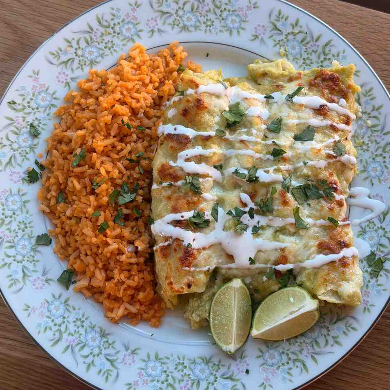 A close-up plate of creamy green chicken enchiladas topped with melted Monterey Jack cheese, queso fresco, and cilantro, served with rice.